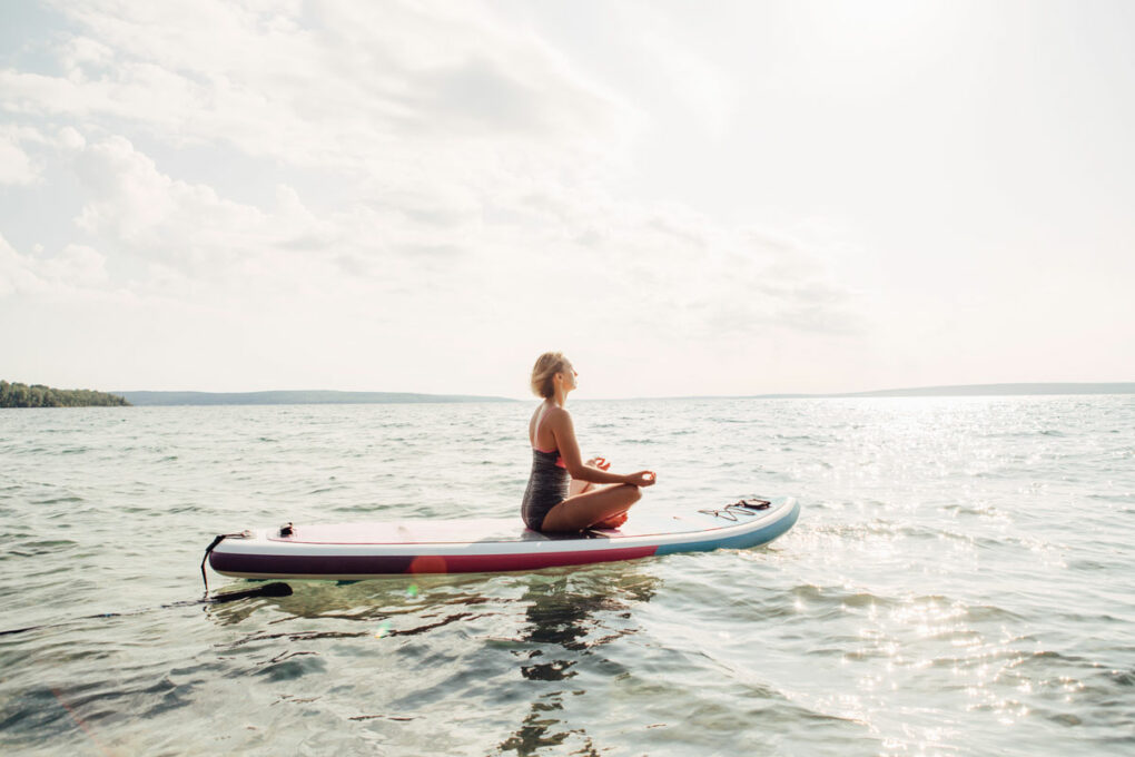 Frau meditiert auf ihrem SUP Board auf dem Wasser